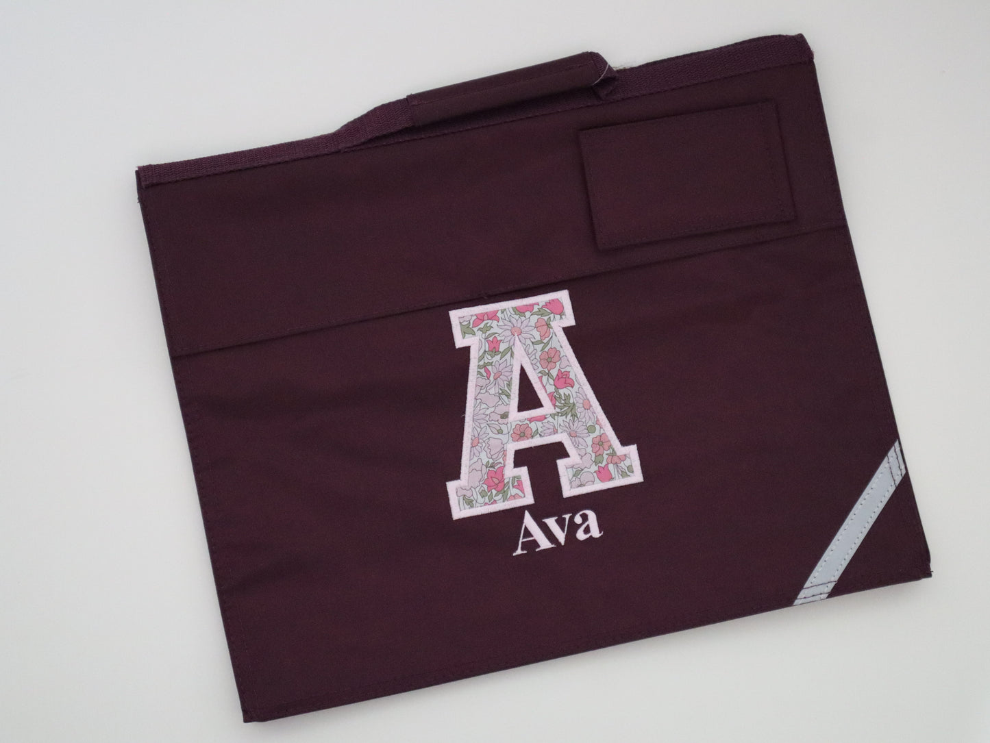 Maroon book bag with floral letter 'A' and name 'Ava'
