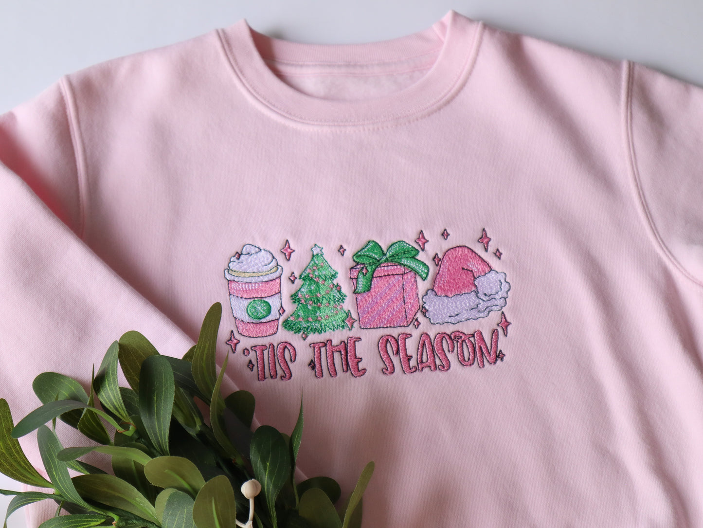 Tis the season kids pink embroidered sweater featuring a christmas design of a christmas tree, Latte, christmas gift and santa hat with the words tis the season