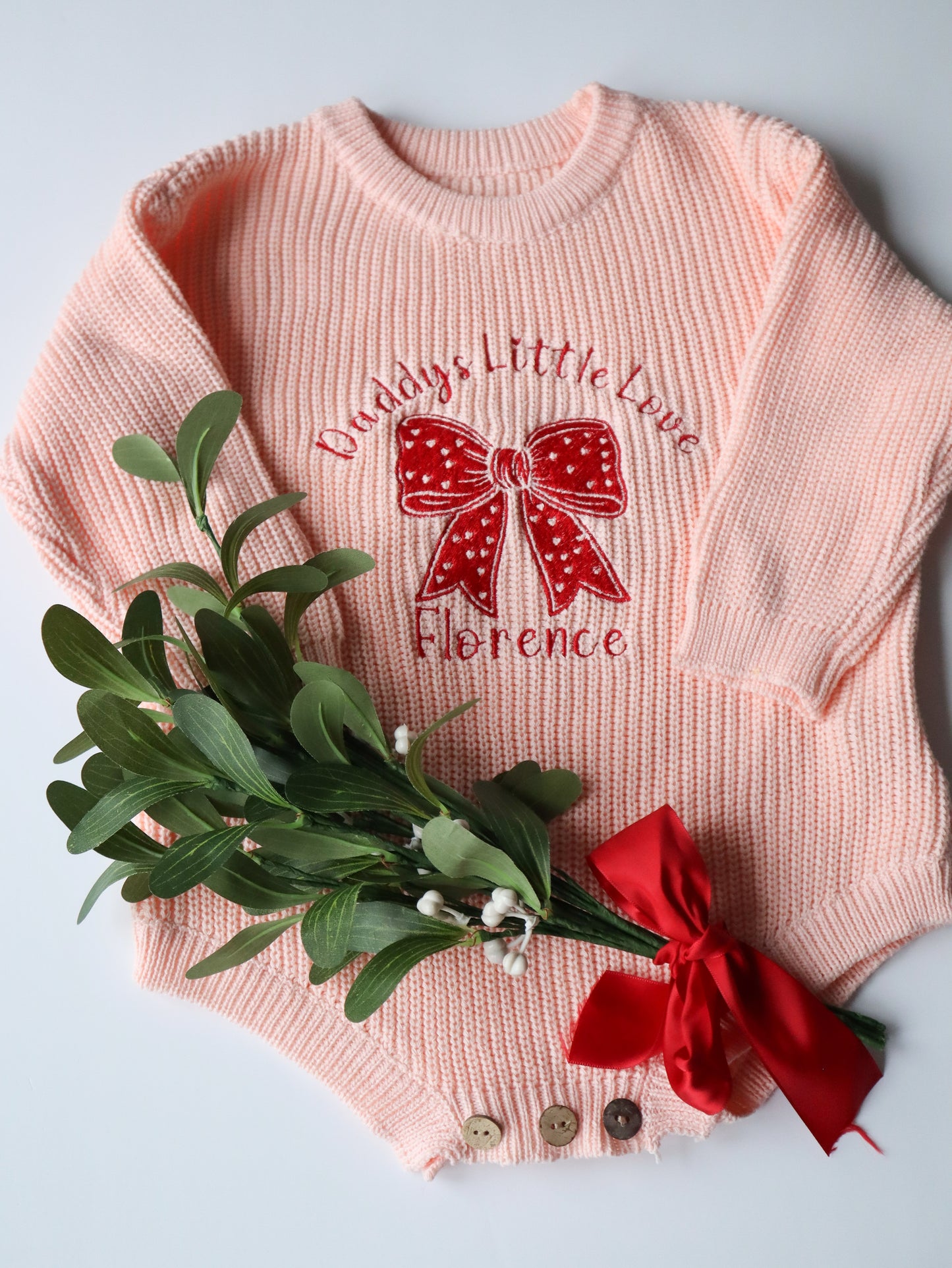 Pink knit romper with an embroidered bow and the words Daddys little love with personalisation of the babies name