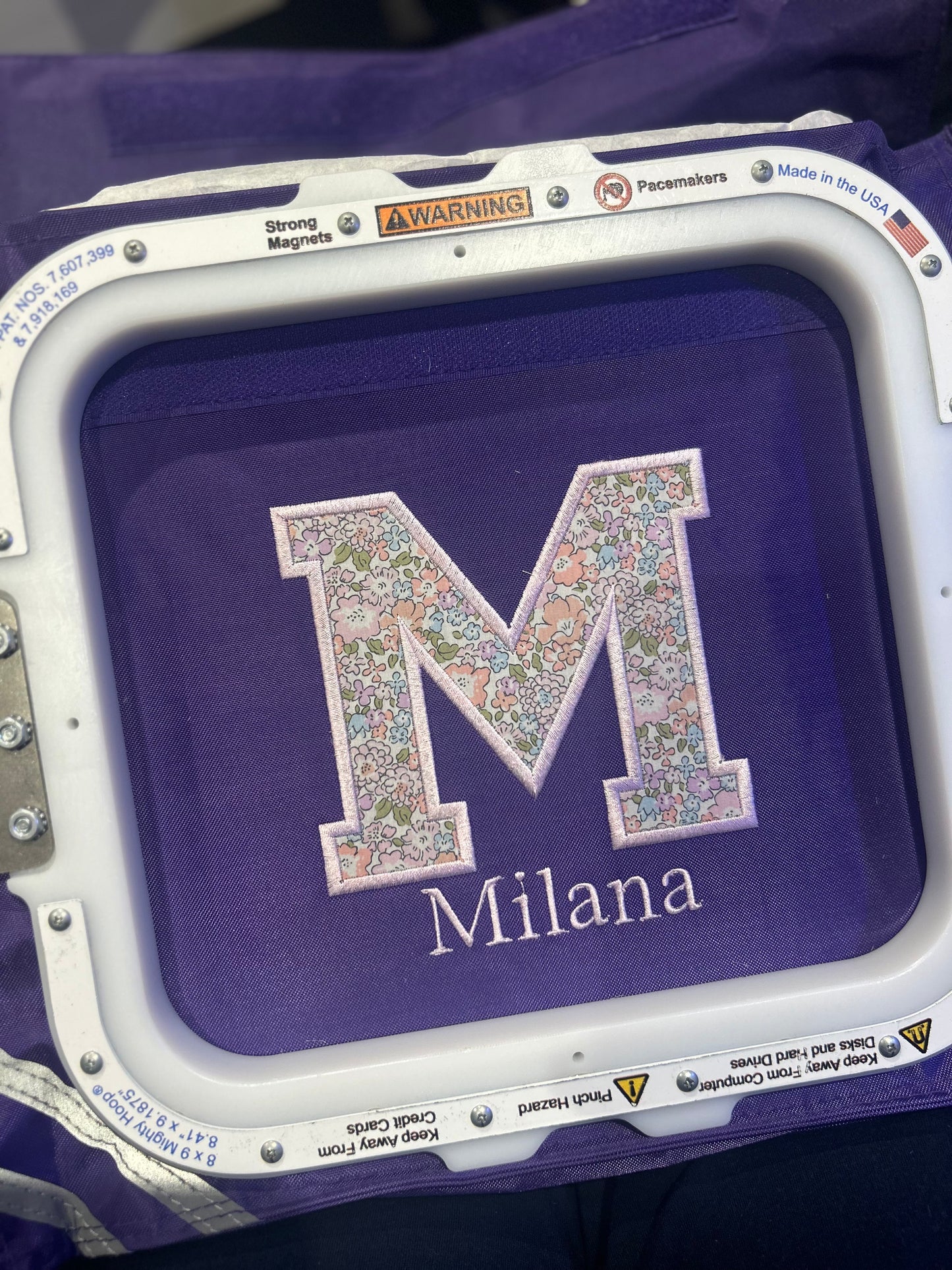 Embroidery hoop with a floral letter 'M' and name 'Milana' on a purple Book Bag