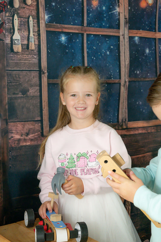 Tis the season kids pink embroidered sweater featuring a christmas design of a christmas tree, Latte, christmas gift and santa hat with the words tis the season
