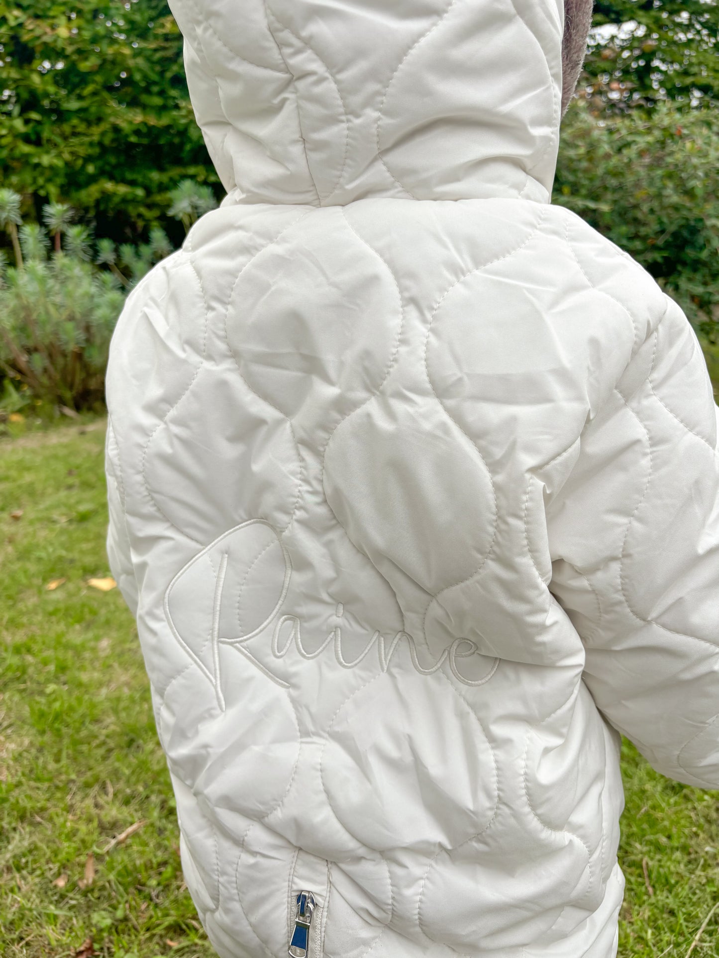White quilted jacket with a Embroidered name on the back, worn outdoors.