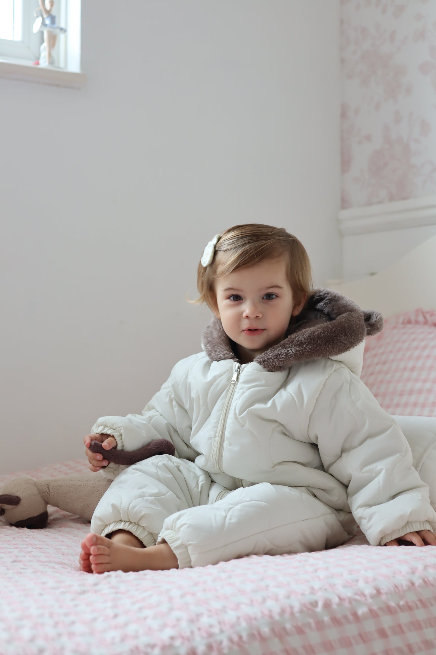Child in a white coat with fur trim lying on a pink blanket