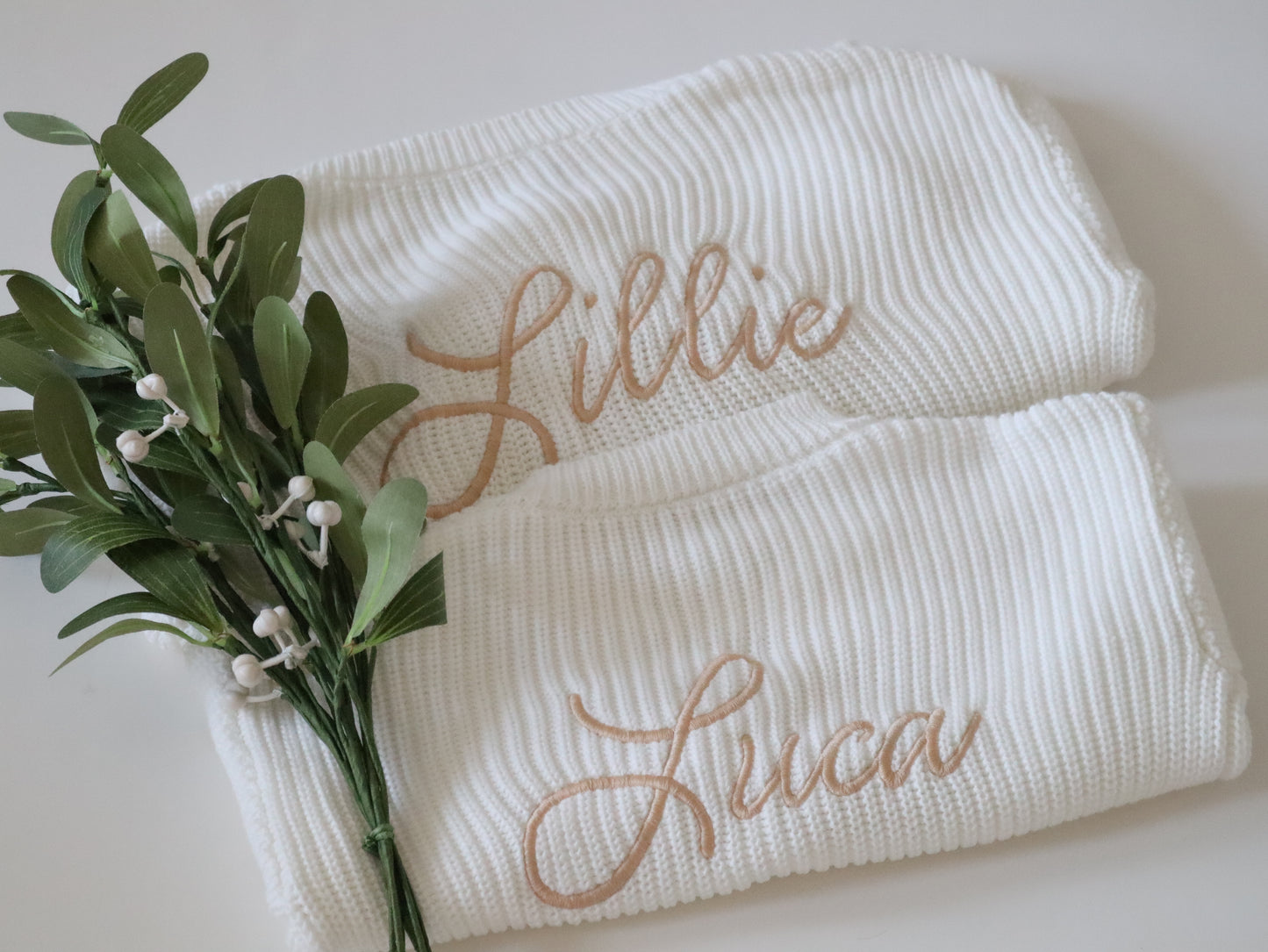 Two white baby cardigans with embroidered names 'Lillie' and 'Luca'