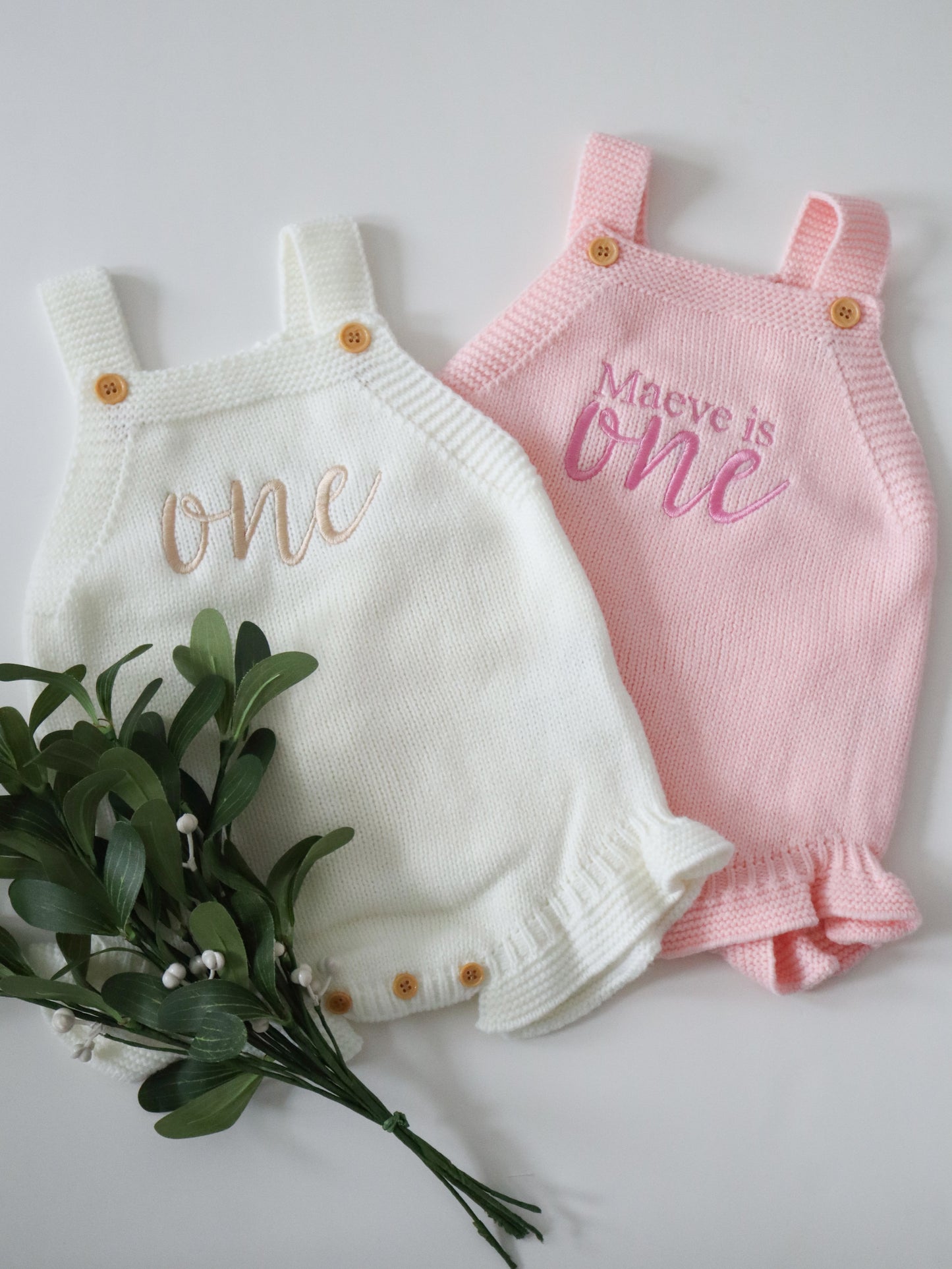 Two baby rompers, one white and one pink, with 'one' and 'Maeve is one' text, on a light background.