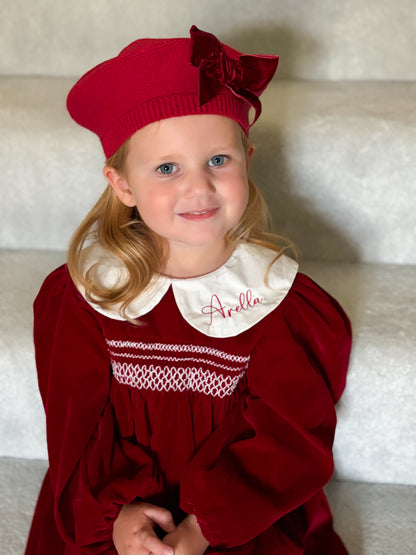 Girl with a red smocked dress with a embroidered with her name white collar 