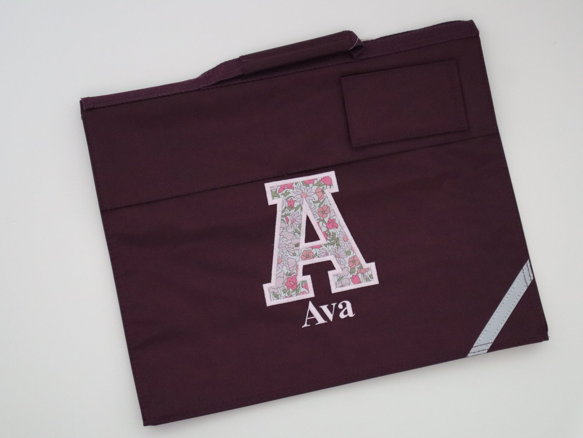 Maroon book bag with floral letter 'A' and name 'Ava' 