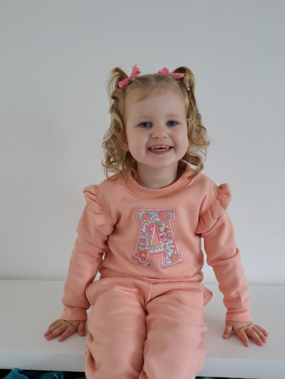 Child wearing a pink outfit with a floral letter 'A' on a white background