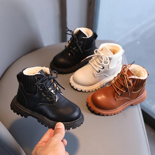A collection of lace-up winter boots in black, white, and brown colors, fur-lined and displayed on a surface with a person's hand reaching out to touch one of the boots.