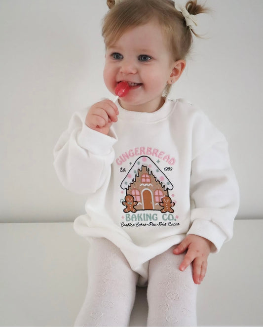 Child wearing a white romper with a gingerbread house design on a plain background