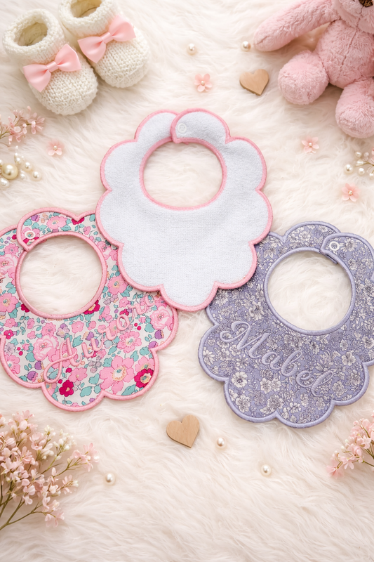 Set of baby bibs with floral patterns on a soft surface with toys and flowers.