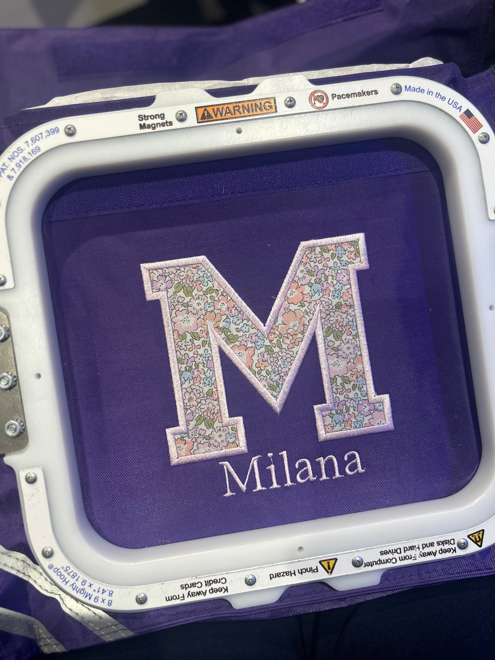 Embroidery hoop with a floral letter 'M' and name 'Milana' on a purple Book Bag