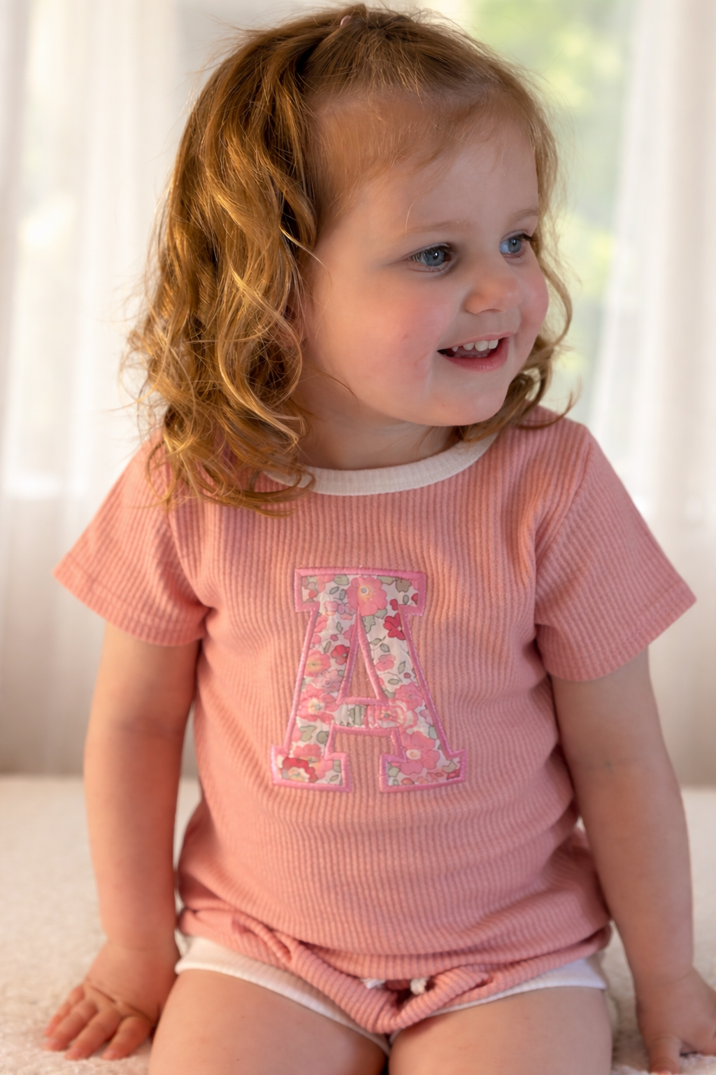 Child wearing a pink outfit with a liberty of london floral letter 'A' design.