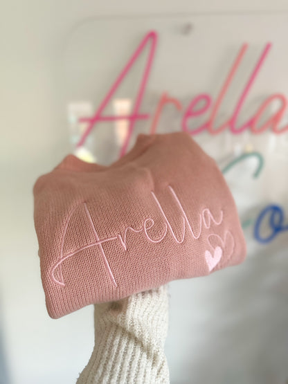 A pink knit frill cardigan with the name 'Arella' embroidered in Pink thread on the Back.