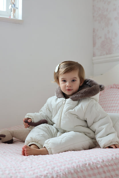 Child in a white coat with fur trim lying on a pink blanket