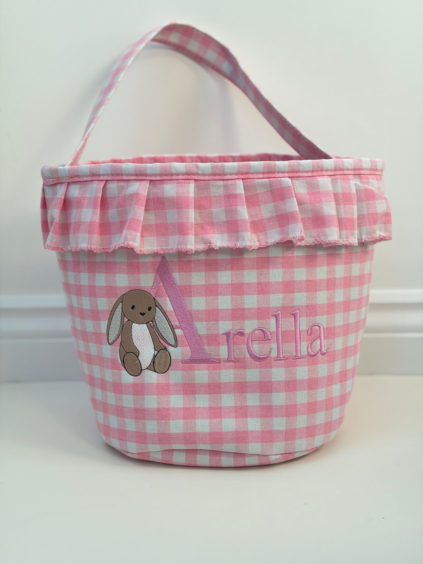 Pink checkered basket with a bunny design and embroidered name on a white background