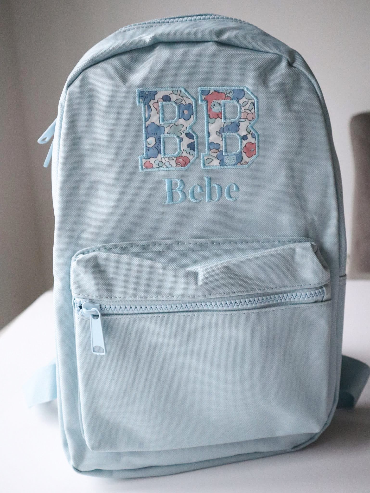 Light blue backpack with floral initials and 'Bebe' text on a neutral background