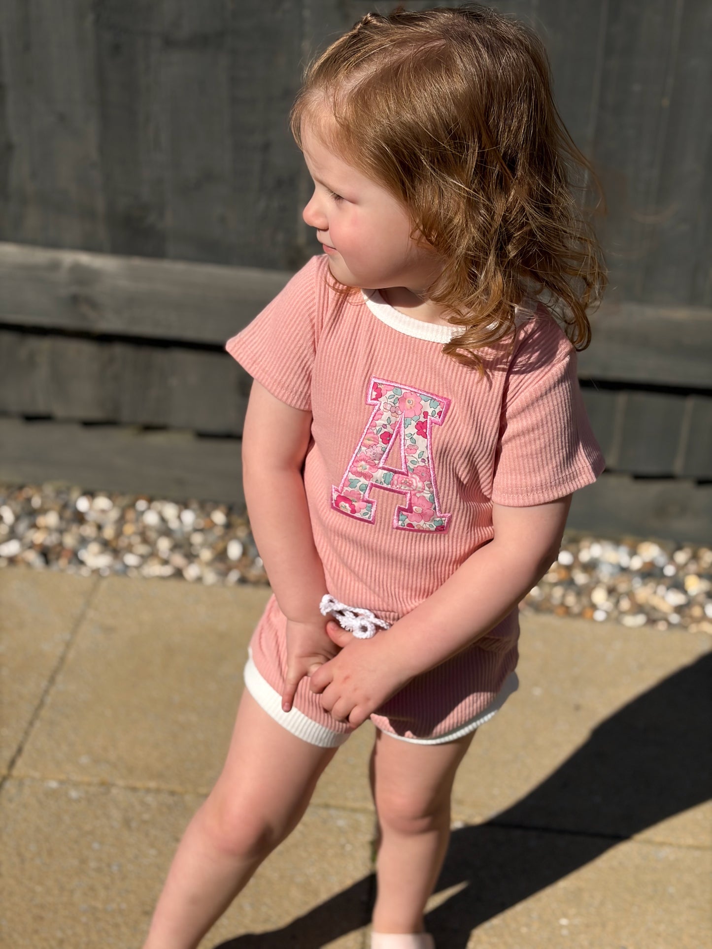 Girl wearing a pink shorts and tshirt set with a floral liberty of london initial A