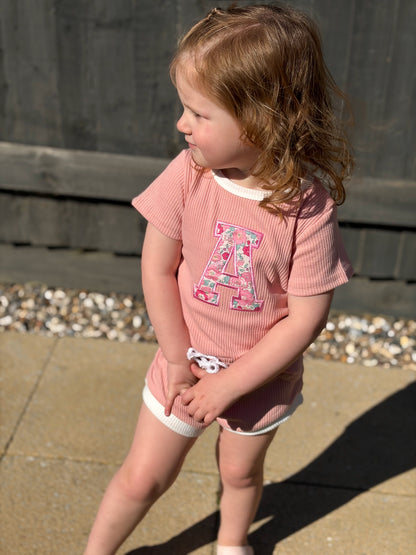 Girl wearing a pink shorts and tshirt set with a floral liberty of london initial A