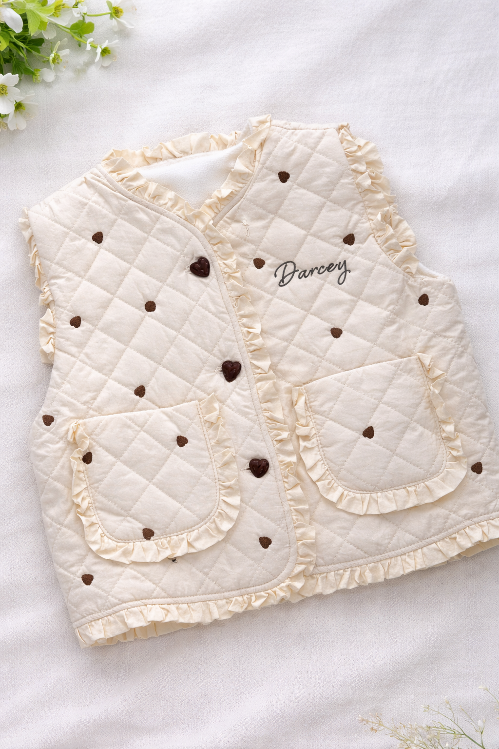 Baby quilted vest with heart patterns and embroidered name on a light background