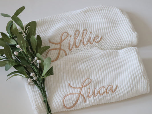 Two white baby cardigans with embroidered names 'Lillie' and 'Luca'