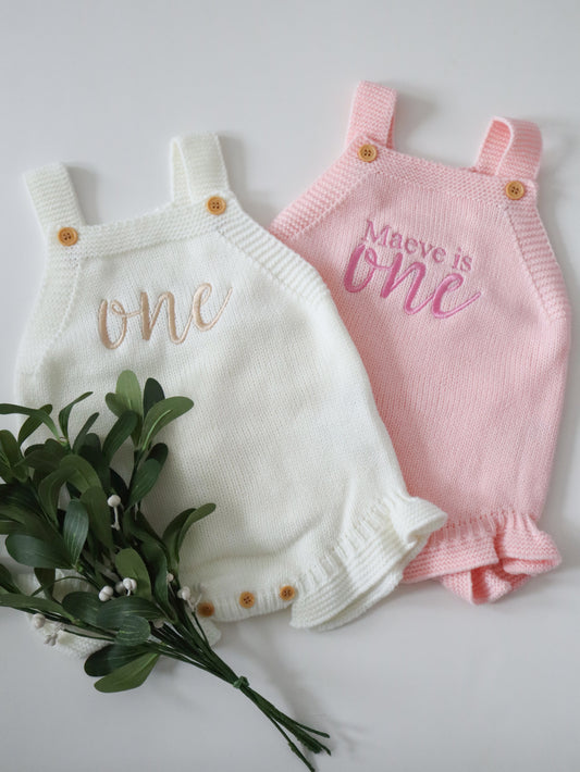 Two baby rompers, one white and one pink, with 'one' and 'Maeve is one' text, on a light background.