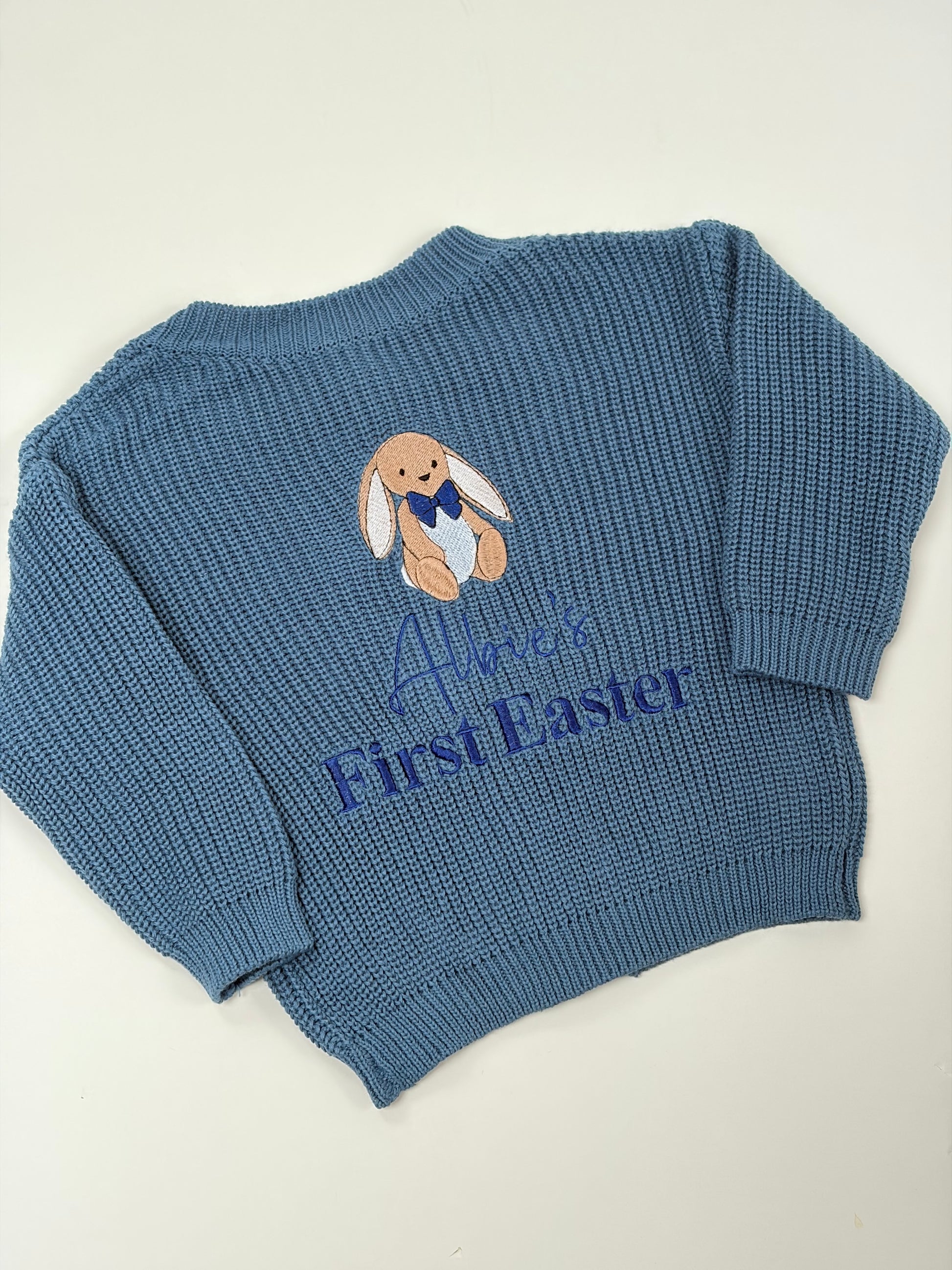 Blue knitted sweater with embroidered bunny and 'Albie's First Easter' text on a white background
